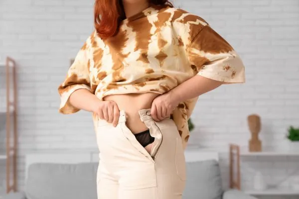 Image of woman trying to do her trousers up after pregnancy weight gain Redditch