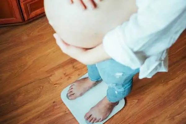 Image of woman weighing herself and experiencing weight gain through pregnancy Redditch